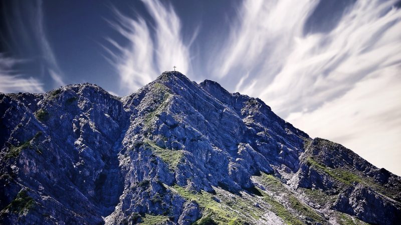 rugged mountains with cross at the peak; blue sky with whisky white clouds